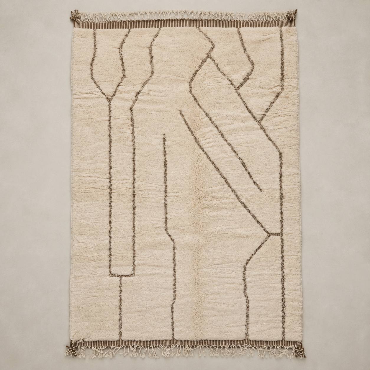 A rectangular cream-colored rug with a textured, hand-tufted abstract pattern in dark brown and fringed edges, shown flat against a neutral light gray background.