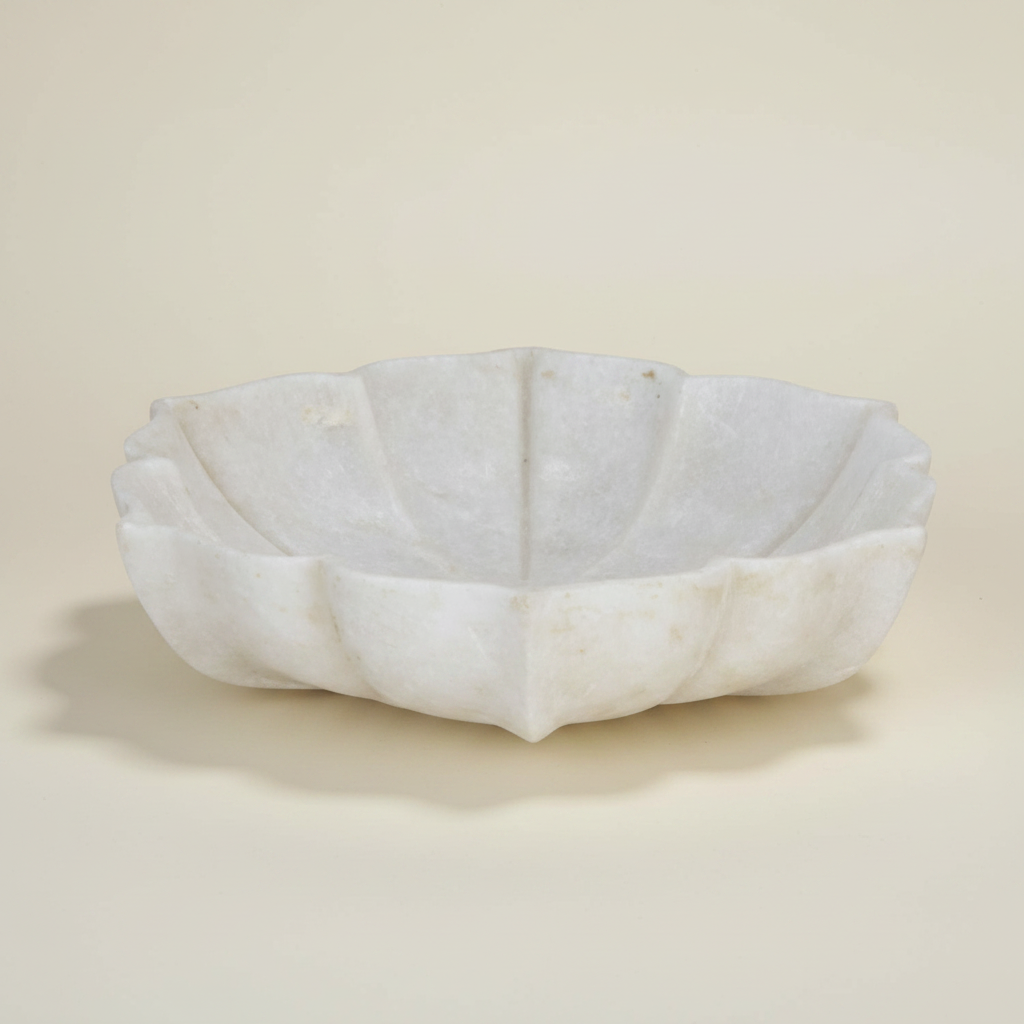 A white marble wall bowl with a scalloped, lotus-like rim, mounted on a textured beige plaster wall.