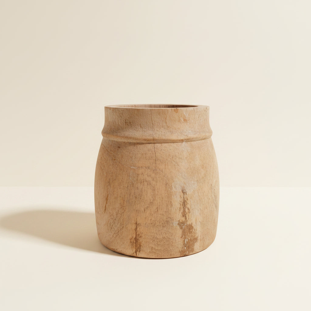 A rustic, hand-carved wooden planter pot with a natural light brown wood finish and visible grain, set against a plain off-white background.