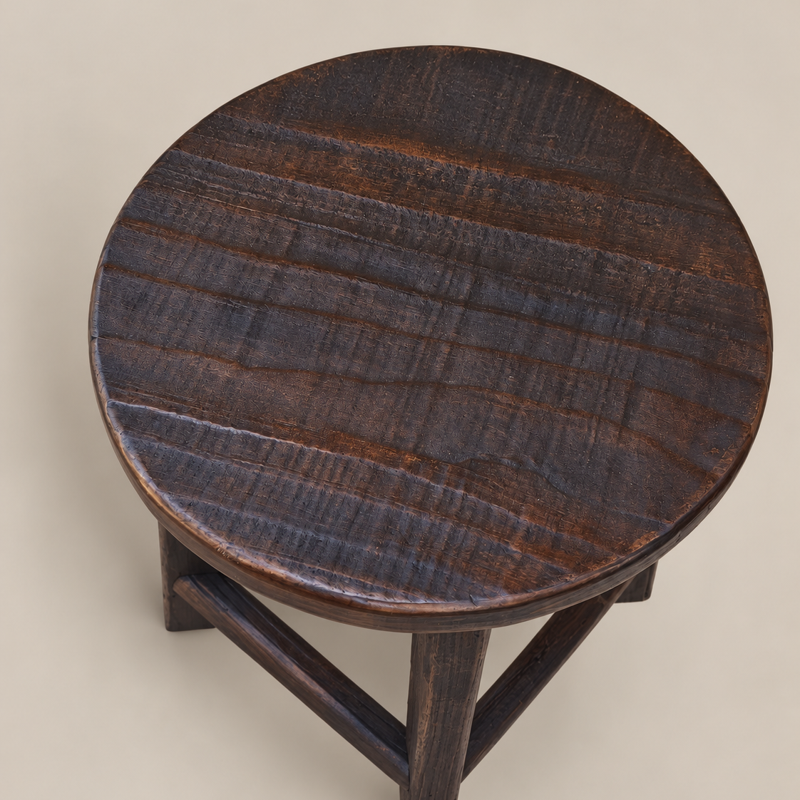 A dark brown wooden stool with a round seat and three angled legs, photographed from a top-down angle against a solid beige background.