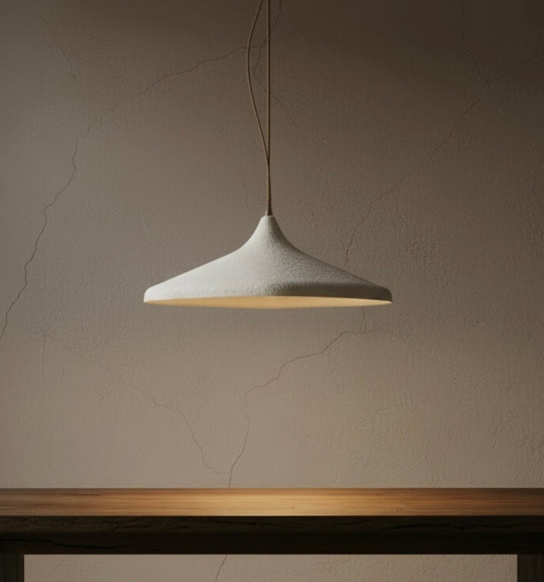 A shallow cone pendant light with a 100cm wide, shallow conical shade hangs above a dark wooden table against a textured beige wall.
