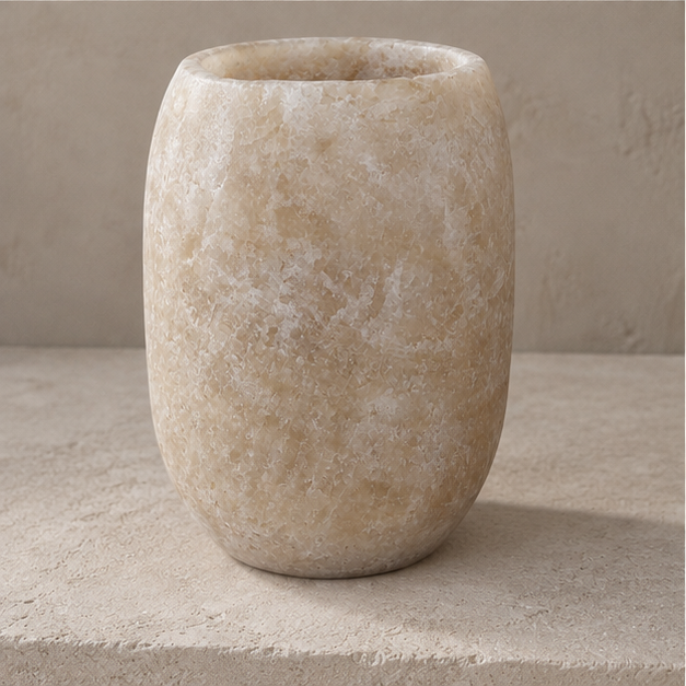 A small rounded stone vase in a warm beige and cream marbled finish, set on a textured stone surface against a matching neutral background.