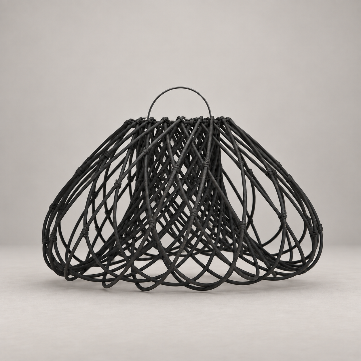 A black woven rattan or wicker basket with a single loop handle, photographed against a neutral light gray studio background.