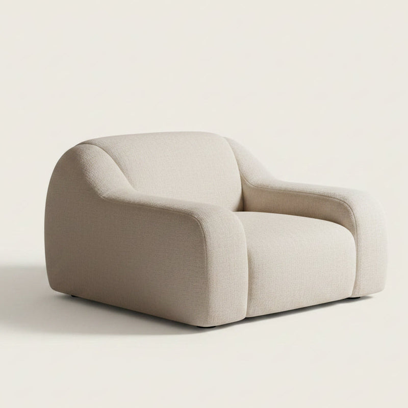 A modern low-profile armchair with a rounded, sculptural design upholstered in an off white upholstered fabric.