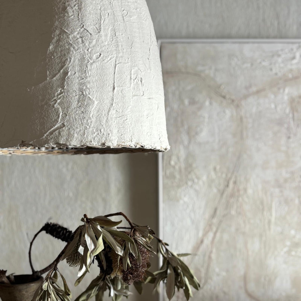 Textured white lampshade with a plant against a neutral wall