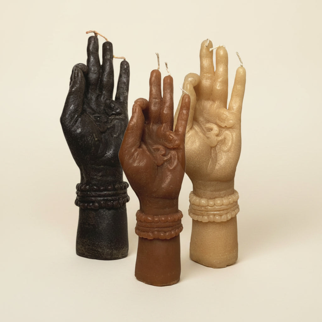 Three hand-shaped candles in black, brown, and beige on a textured white background