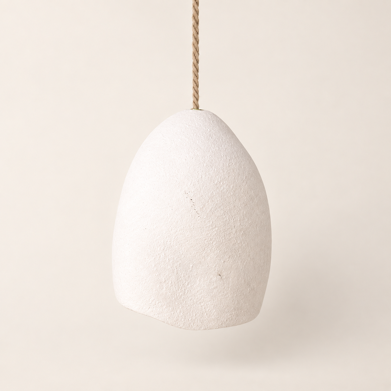 A textured off-white ceramic pendant light shade suspended by a natural jute rope cord against a warm cream background.