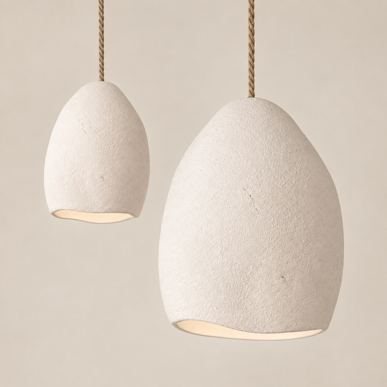 Two textured pendant light shades in a warm off-white stone-like finish, suspended by twisted natural-fiber cords against a soft beige background.