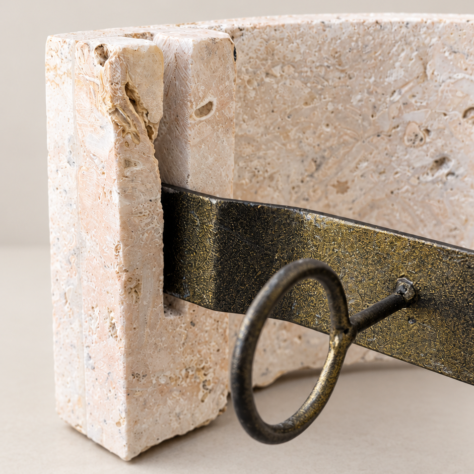 A close-up of a rustic stone block bookend with a dark metal band and hanging ring, set against a neutral beige background.