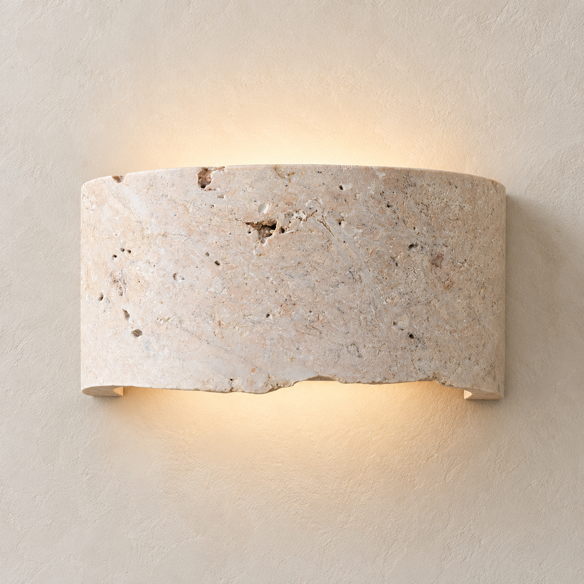 A curved rectangular wall sconce made of natural travertine stone, illuminated from within to cast a warm glow against a textured beige plaster wall.