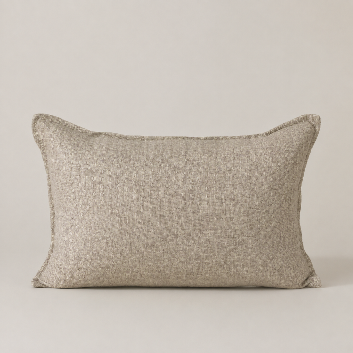 A rectangular lumbar pillow in a textured beige linen fabric, shown against a neutral light beige background.