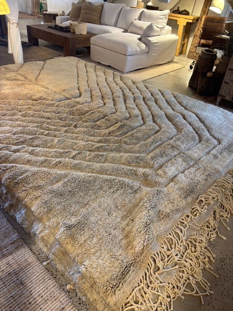 A hand-selected Moroccan Berber rug with a geometric pattern and fringes, displayed in a room setting.