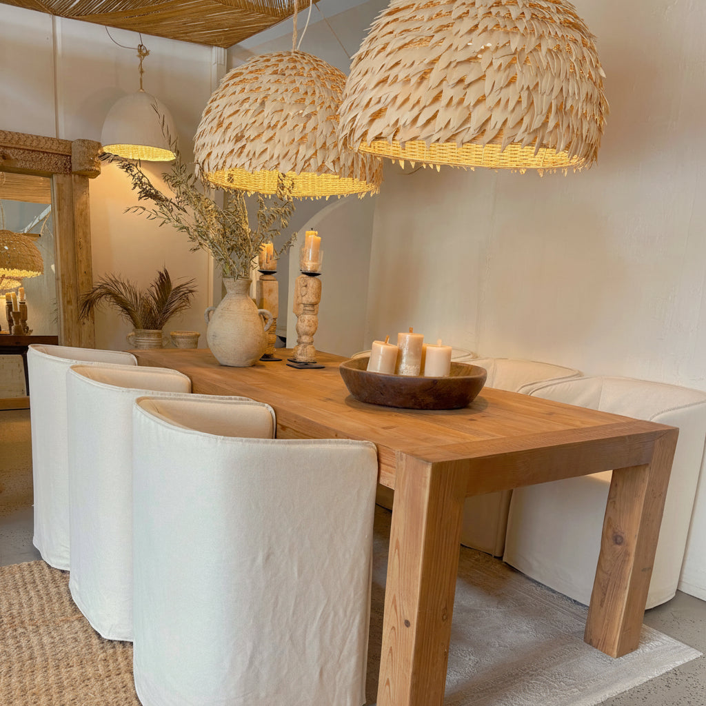 Dining area with wooden table, white chairs, and wicker and coconut pendant lights