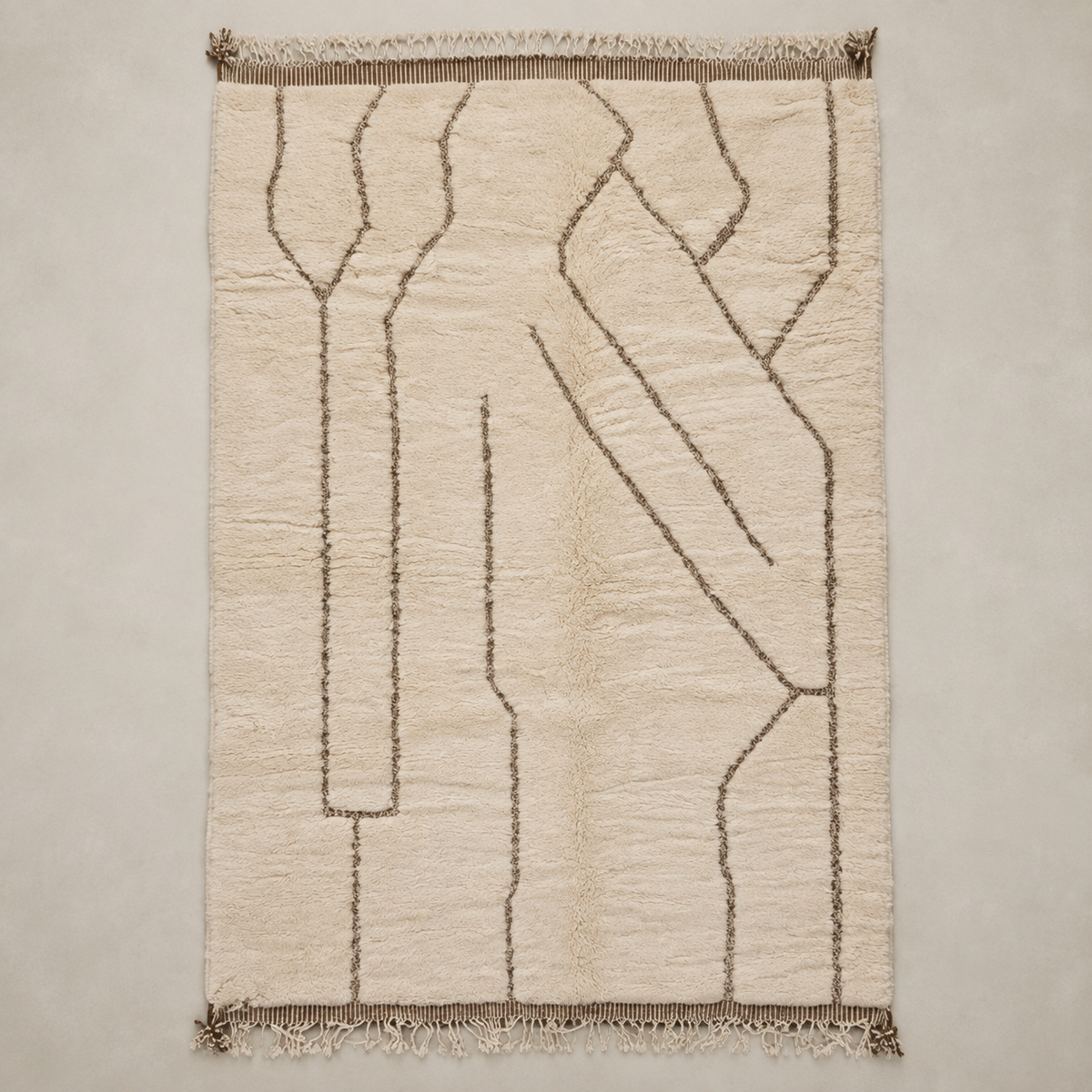 A rectangular cream-colored rug with a textured, hand-tufted abstract pattern in dark brown and fringed edges, shown flat against a neutral light gray background.