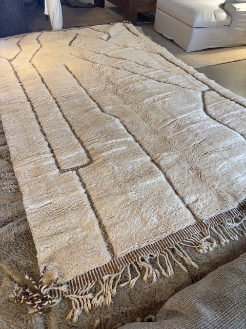 A hand-selected Moroccan Berber rug with a beige and brown color palette, featuring geometric patterns and fringes on the edges.