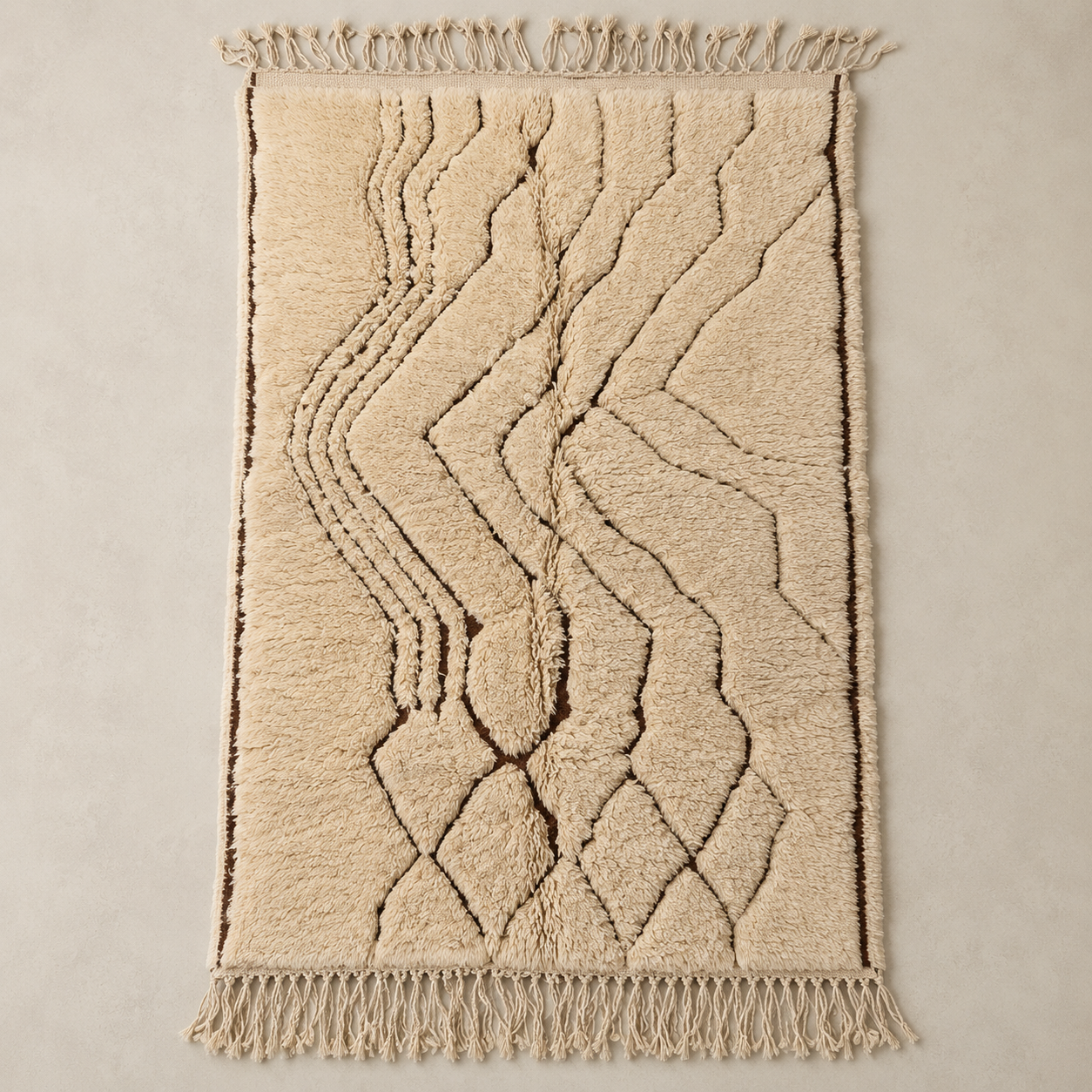 A rectangular beige shag rug with a raised geometric chevron and diamond pattern, finished with fringed edges on the top and bottom, laid flat against a neutral beige background.