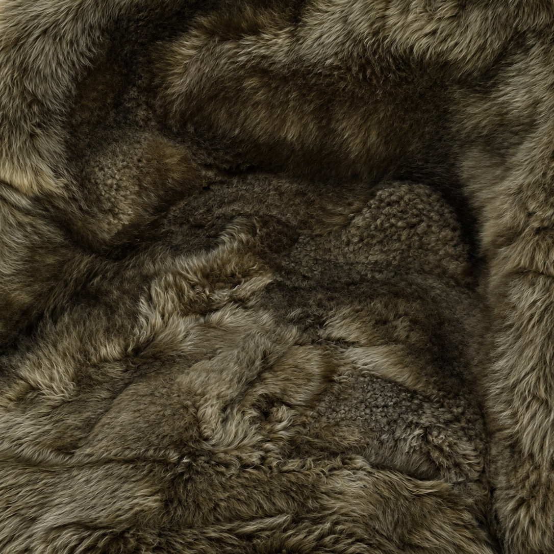 A close-up of a plush faux fur or sheepskin textile with dense, shaggy fibers in mixed taupe, brown, gray, and cream tones.