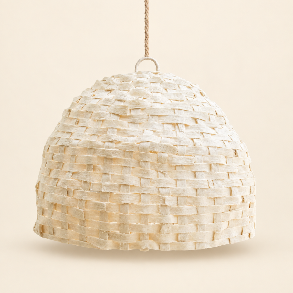 A dome-shaped woven pendant light shade made from natural beige raffia or straw strips, suspended by a twisted rope cord with a metal ring, set against a solid cream background.