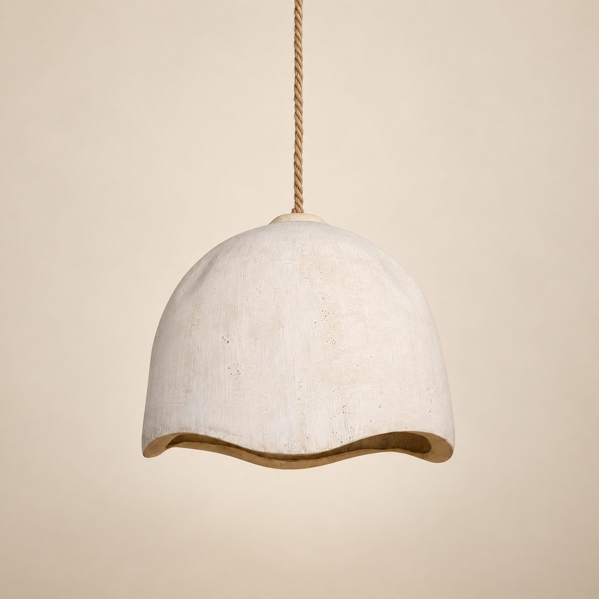 A dome-shaped pendant light with a textured off-white ceramic or stone finish and a wavy lower edge, suspended by a twisted natural-fiber rope against a warm beige background.