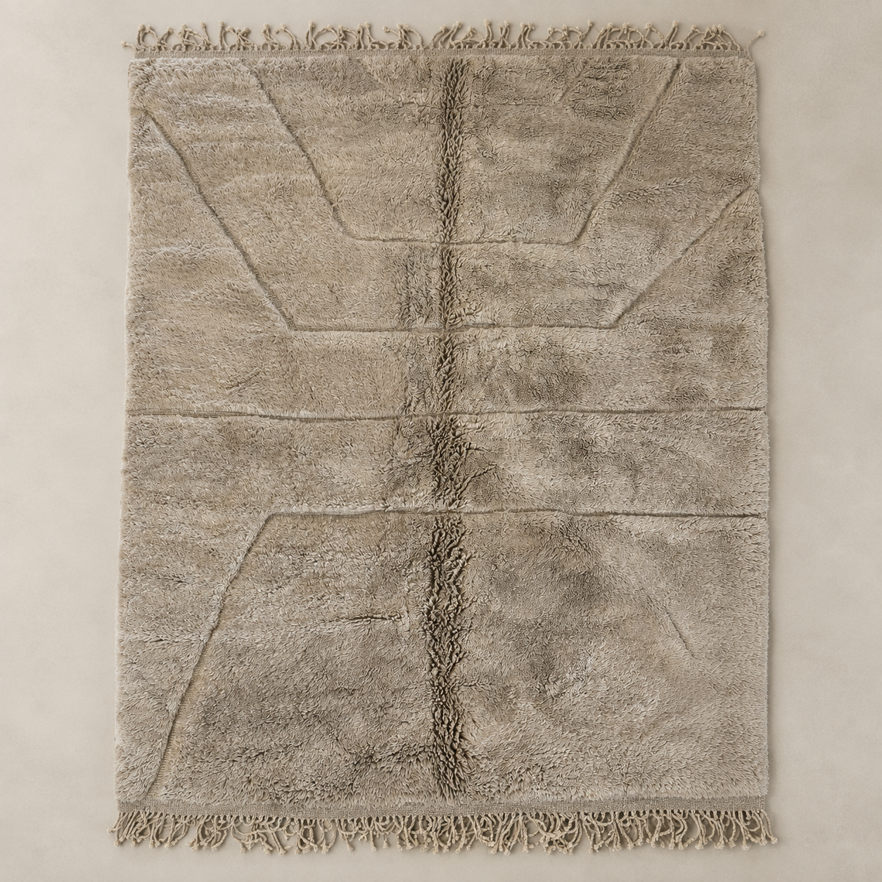A rectangular shag area rug in a warm taupe-beige color, featuring a central vertical channel, geometric line patterns, and fringed edges on the top and bottom, laid flat against a neutral beige background.