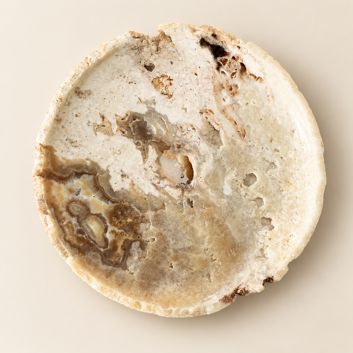 A round, flat stone or ceramic dish with a marbled beige, cream, and brown pattern, photographed from directly above on a light beige background.