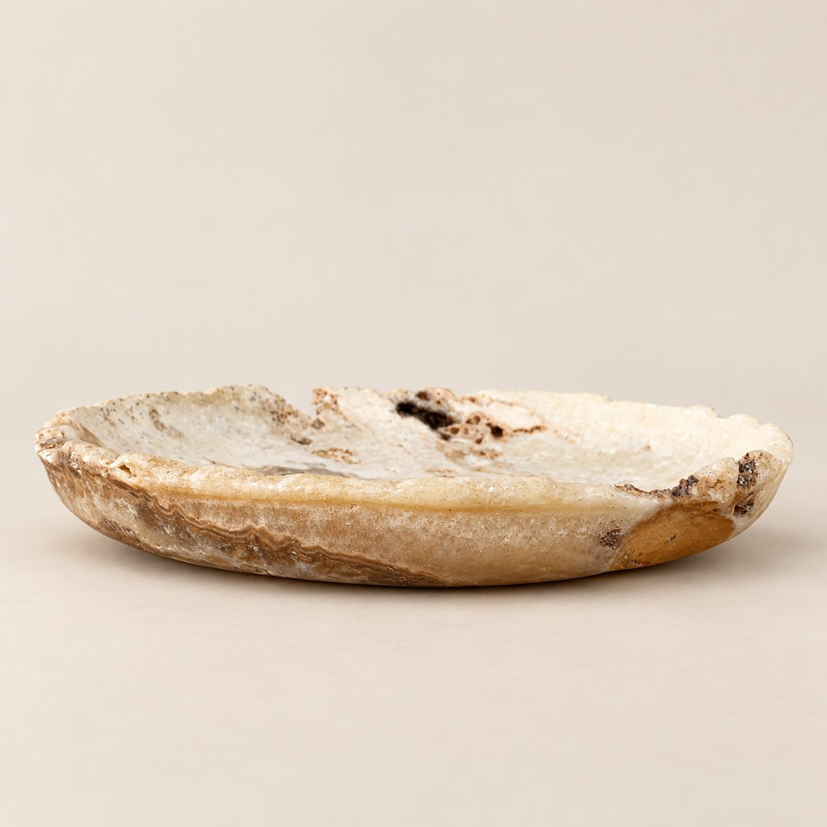 A small, shallow dish carved from natural agate or quartz with a rough, crystalline texture and organic brown and black inclusions, shown on a neutral beige background.