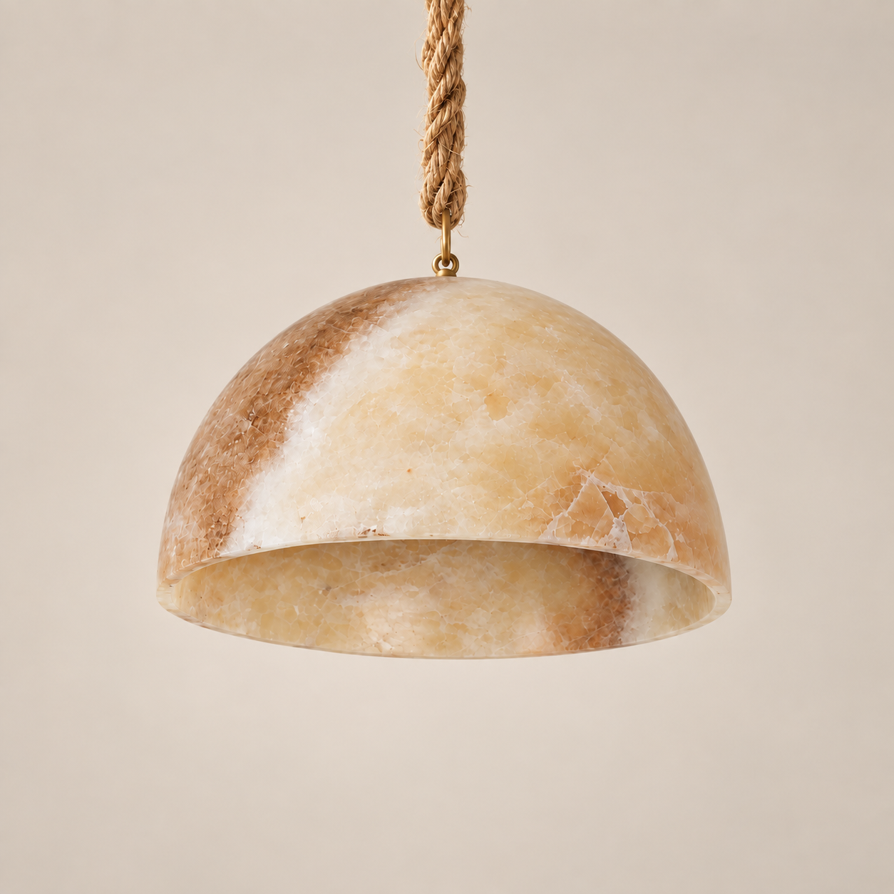 A dome-shaped pendant light shade made of natural beige and brown marbled stone, suspended from a braided rope cord with a brass ring, set against a solid warm beige background.