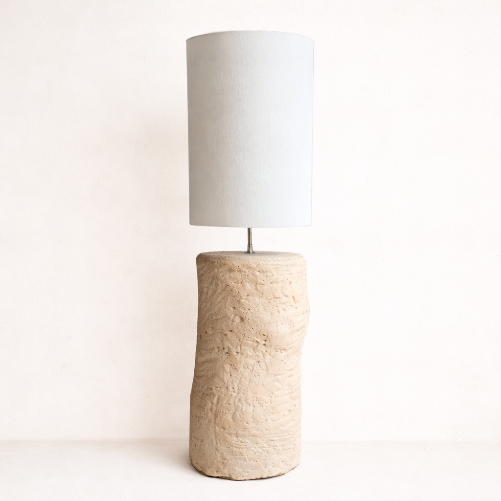 Lamp with textured base and white shade on a light background by Bisque Traders