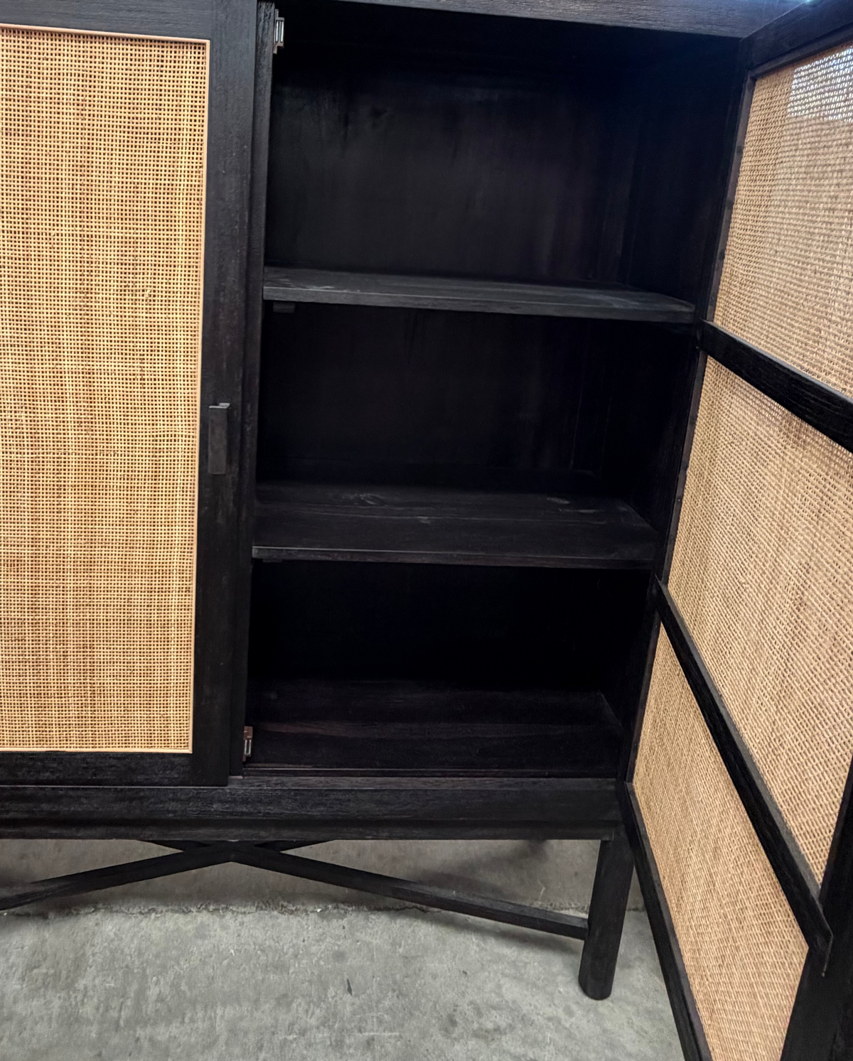 A dark wood cabinet with woven cane or rattan panel doors, shown open with three interior shelves visible.