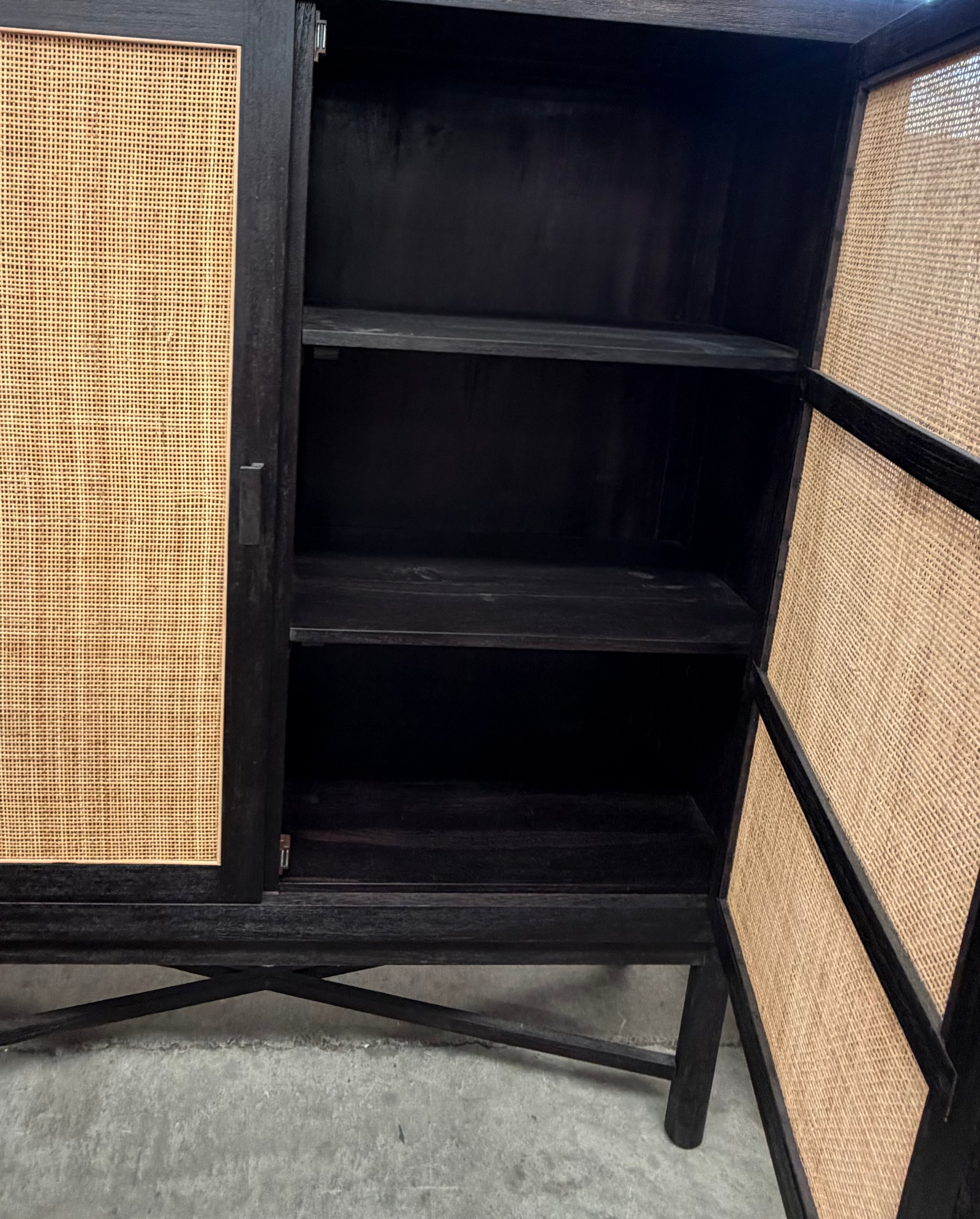 A dark wood cabinet with woven cane or rattan panel doors, shown open with three interior shelves visible.