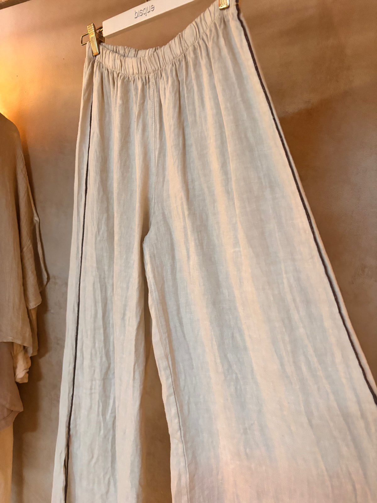 Light-colored pants with a black stripe hanging against a neutral background