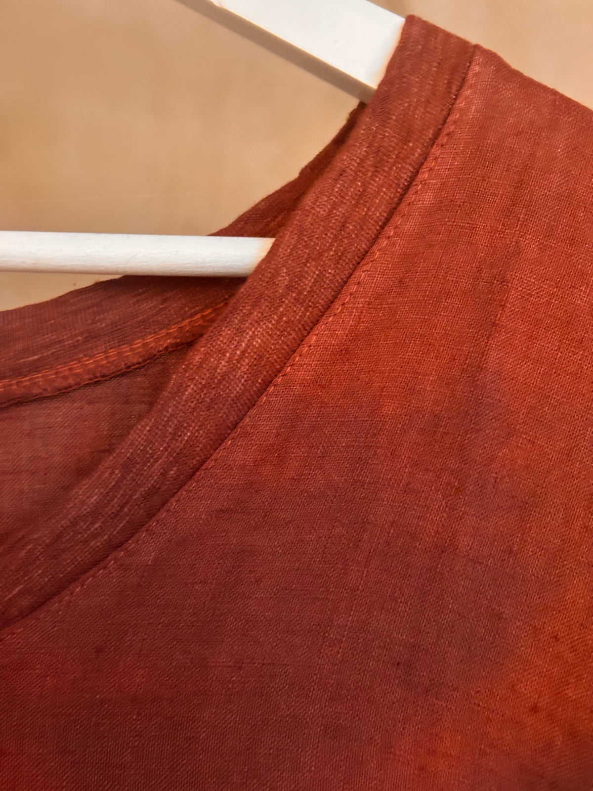 Close-up of a brown Armonia cotton t-shirt garment on a hanger against a beige background