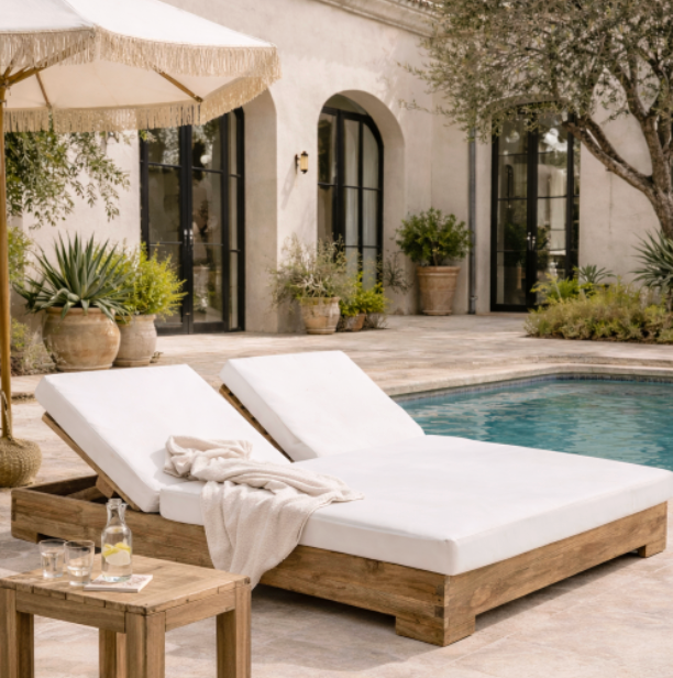 Two white lounge chairs with wooden legs by a poolside, with a beige umbrella and small table.