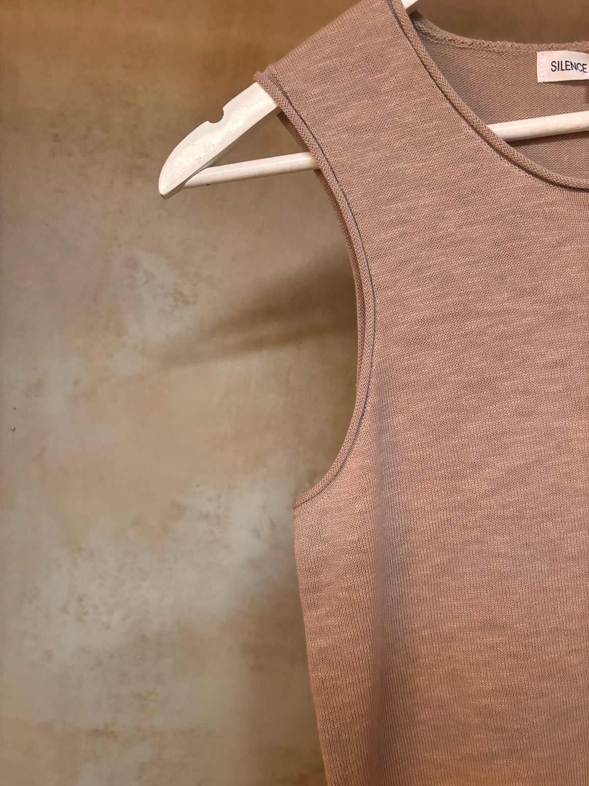 Brown pure linen knit tank top on a hanger against a textured beige wall
