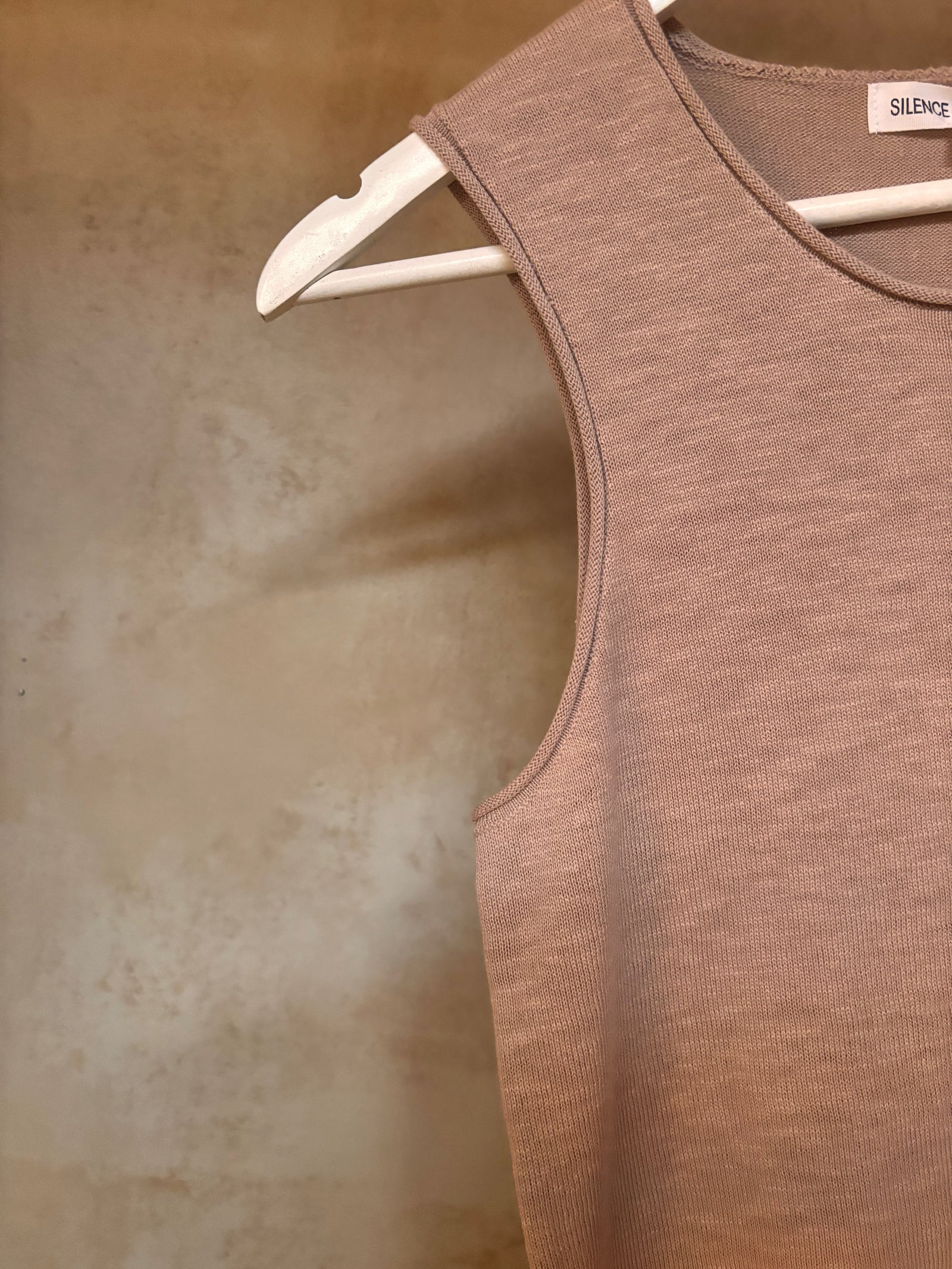 Brown pure linen knit tank top on a hanger against a textured beige wall