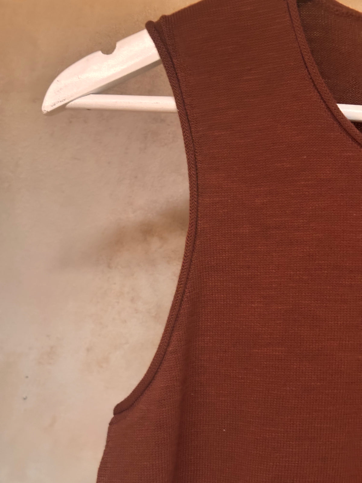 Brown sleeveless pure cotton knit top on a hanger against a beige background