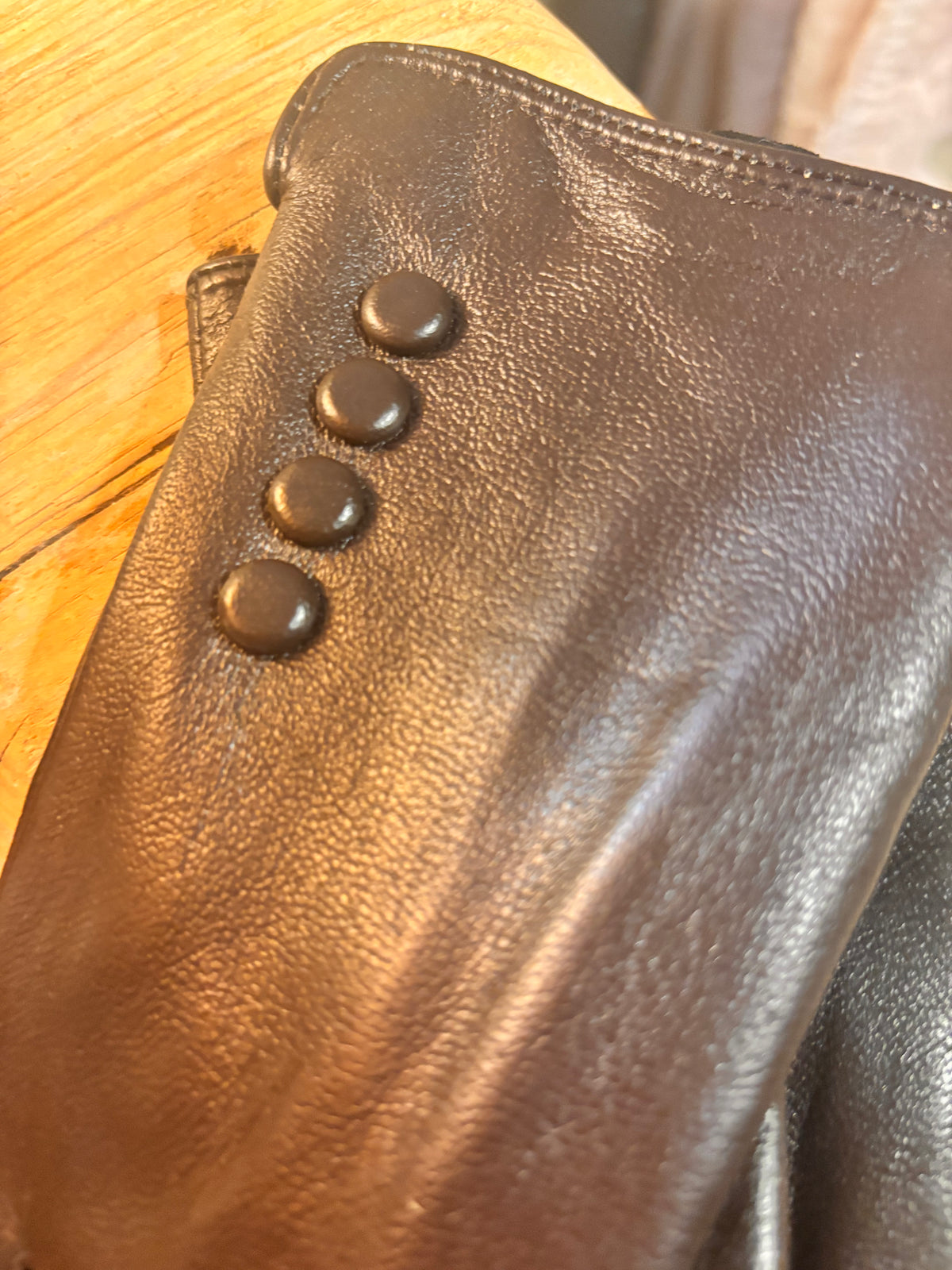 Close-up of a brown leather bag with three buttons on a wooden surface