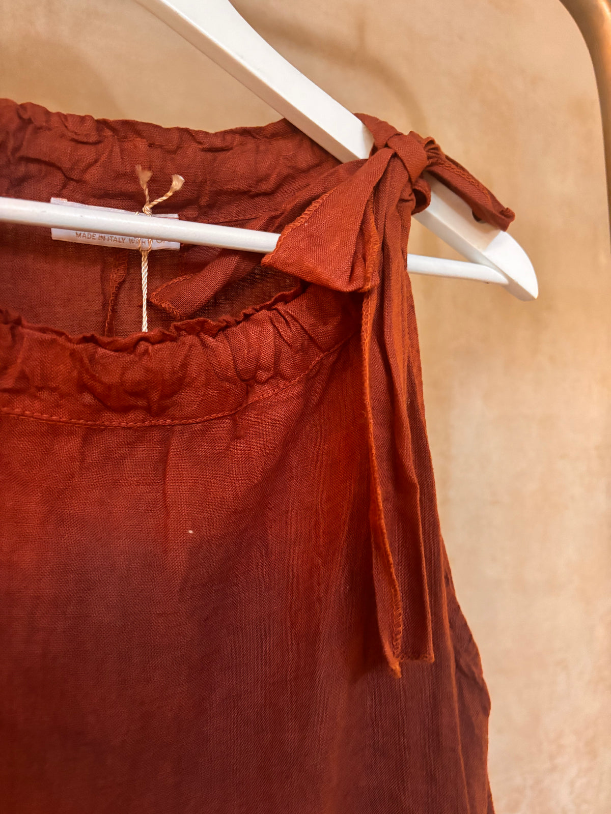 brown top with ruffles and a bow detail on a hanger against a beige background