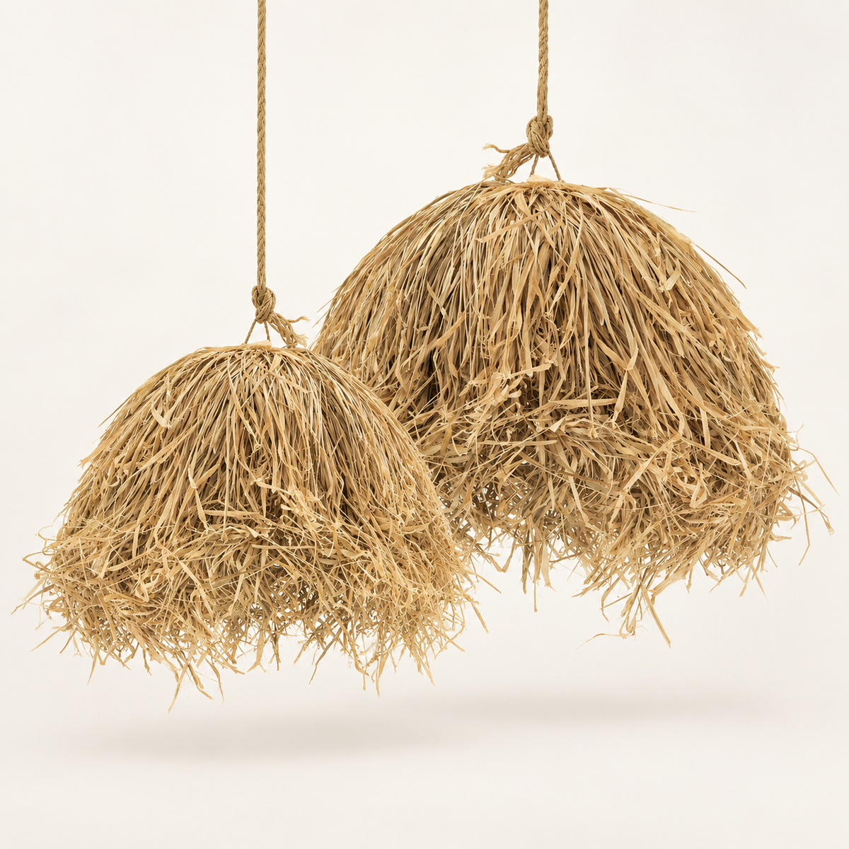 Two hanging pendant lights made from natural straw or raffia fiber, suspended from tan cords against a clean off-white background.