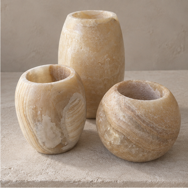 Three small stone vases in warm beige and cream tones with natural marbled texture, arranged on a stone surface against a matching neutral background.