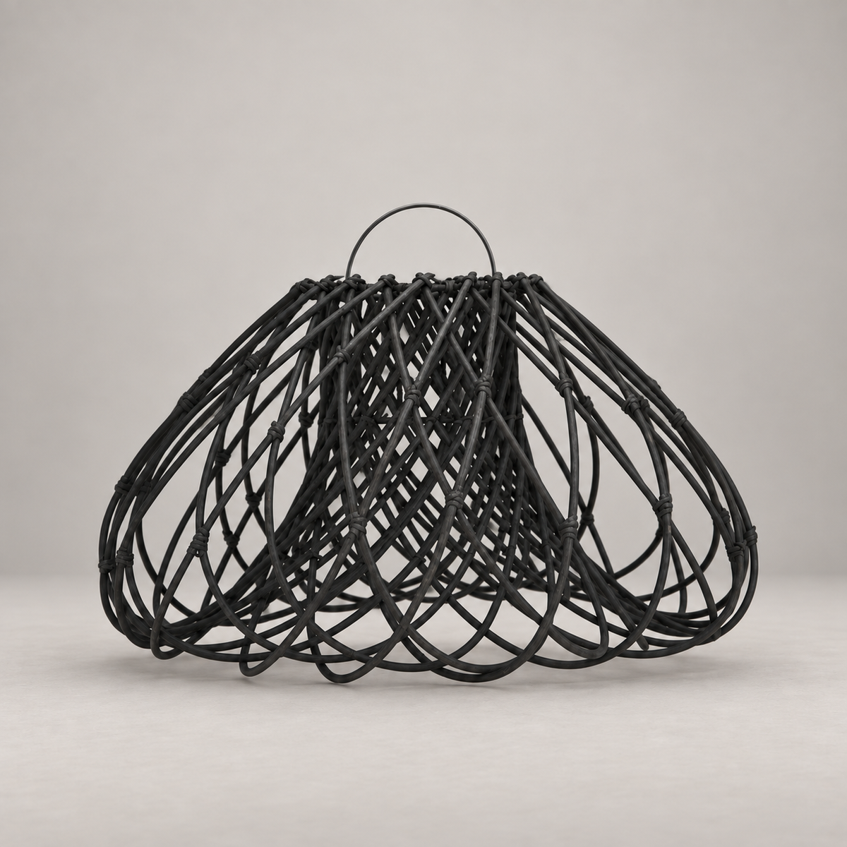 A black woven rattan or wicker basket with a single loop handle, photographed against a neutral light gray studio background.