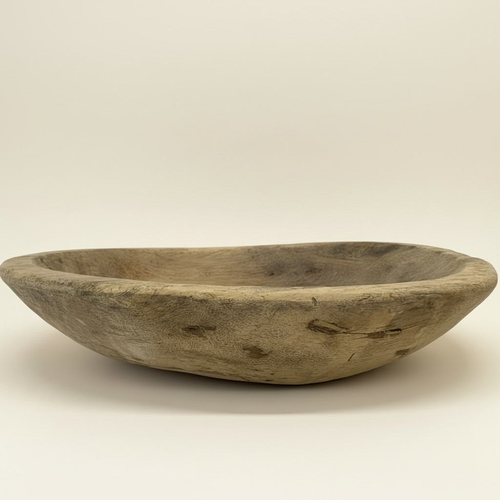 A rustic oval wooden bowl with a natural weathered finish, styled with green fern fronds inside, set against a solid warm beige background.