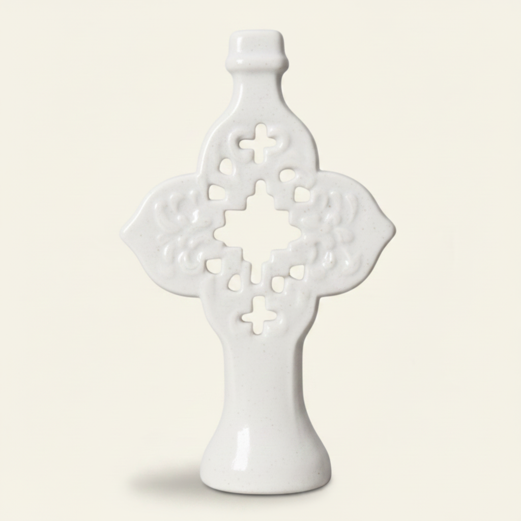 A distressed white ceramic Celtic cross figurine with brown speckled accents, shown on a light cream background.