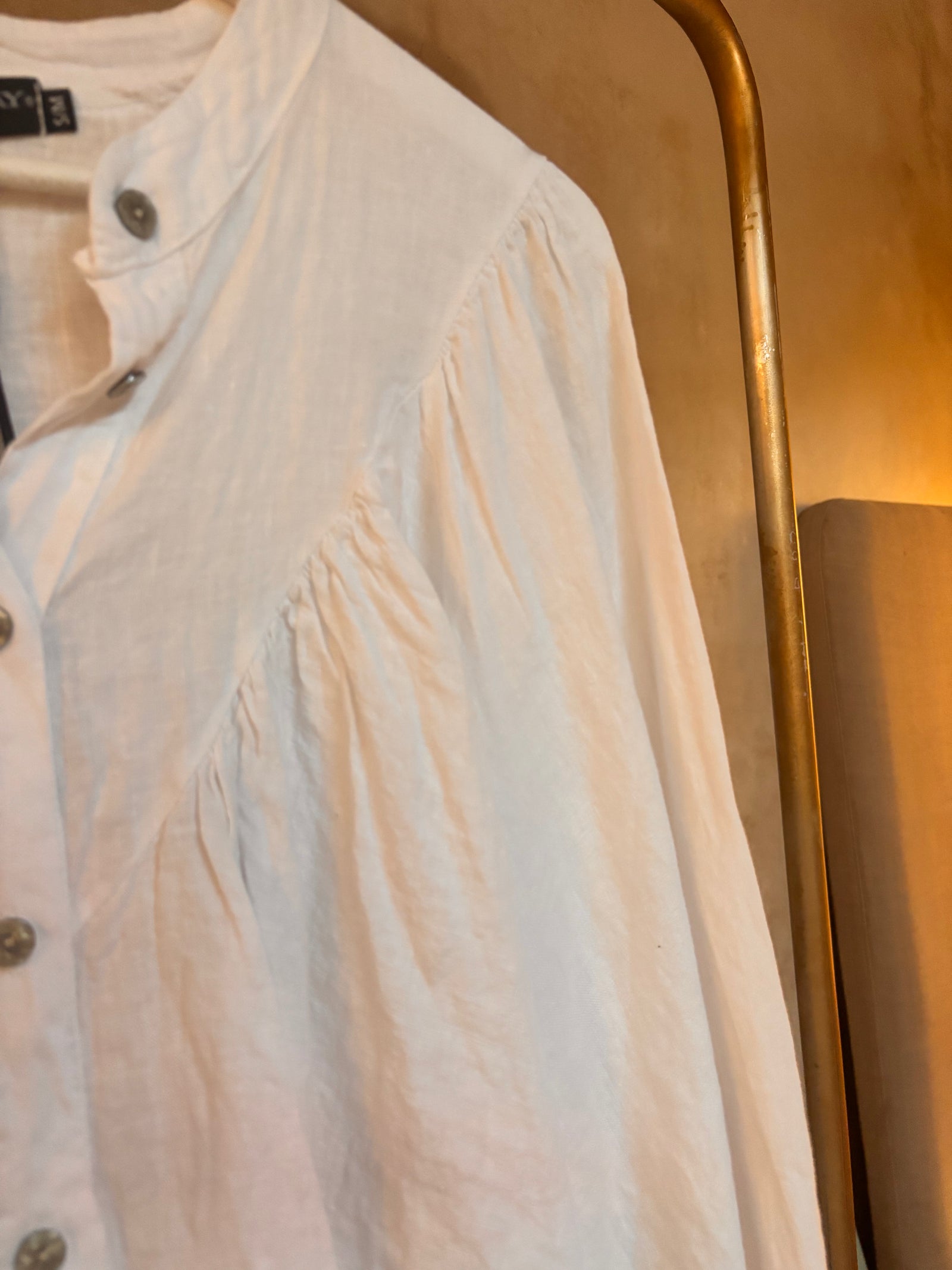 White Italian linen shirt on a hanger against a gold background