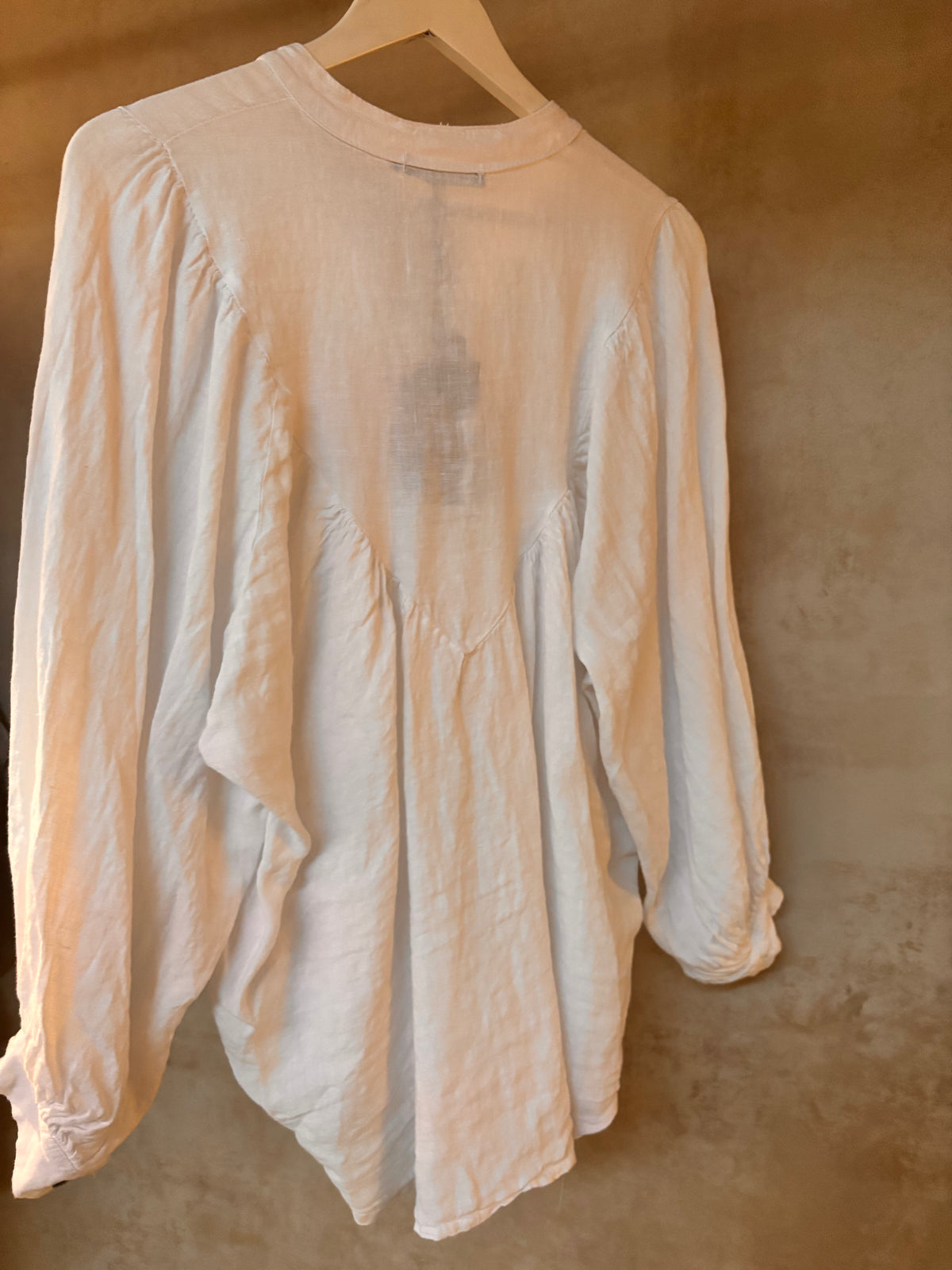 White Italian Linen long-sleeve shirt on a hanger against a textured wall.