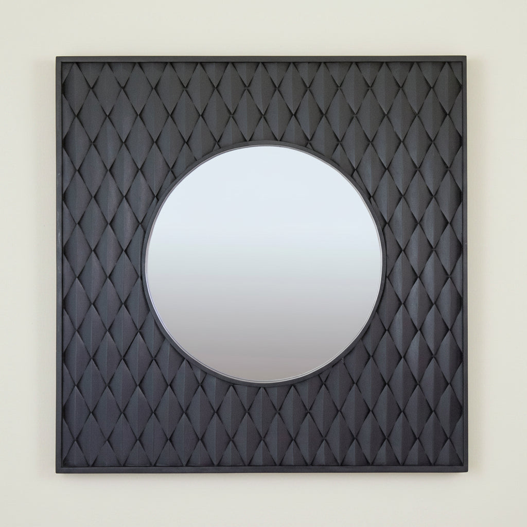 A square wooden mirror with a raised diamond design frame in a black washed finish, with a round mirror at the center.