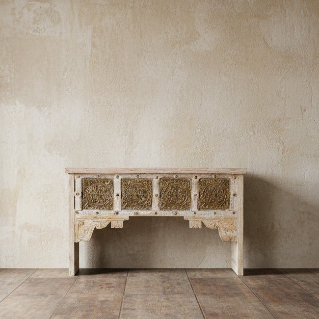 A wooden console table with a whitewashed finish, featuring recycled brass panels and old wood, with intricate brass detailing.